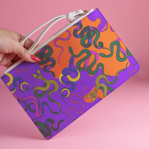 Rectangular wristlet clutch featuring vibrant purple and orange background with colorful snake prints. White strap and gold zipper visible.
